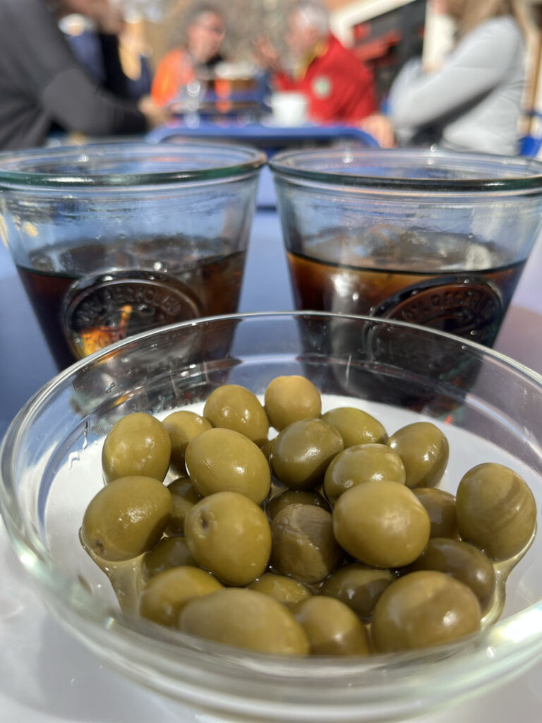 Ein Schälchen grüner Oliven und zwei Gläser mit rotem Wermut.