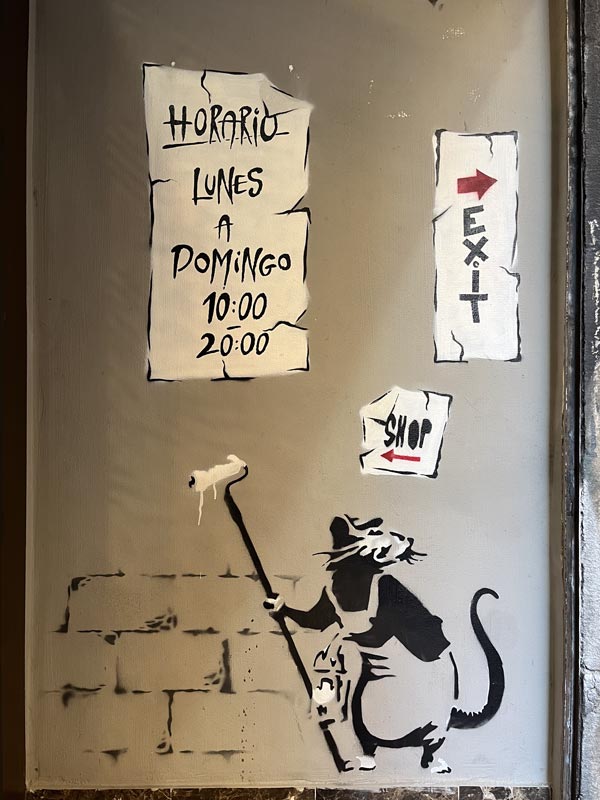 Ein Schild mit den Öffnungszeiten des Bansky Museum, mit einer Ratte, die einen Farbpinsel und Farbeimer in der Hand hält.