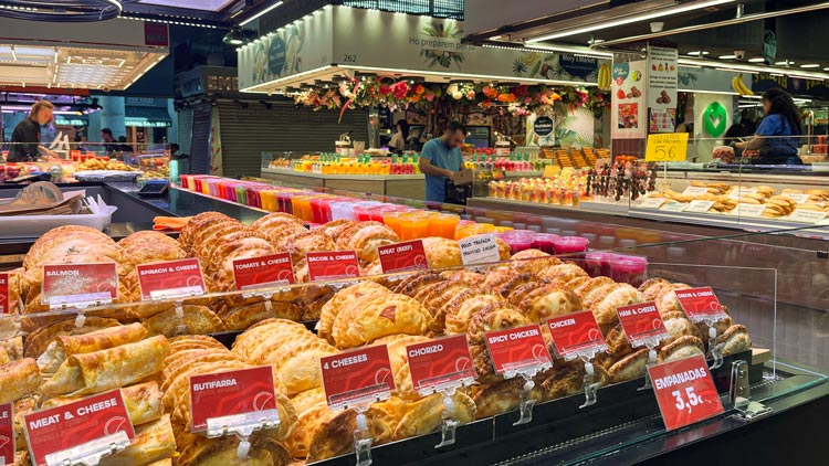 Ein Marktstand der Boqueria mit Empanadas und Fruchtsäften im Angebot.